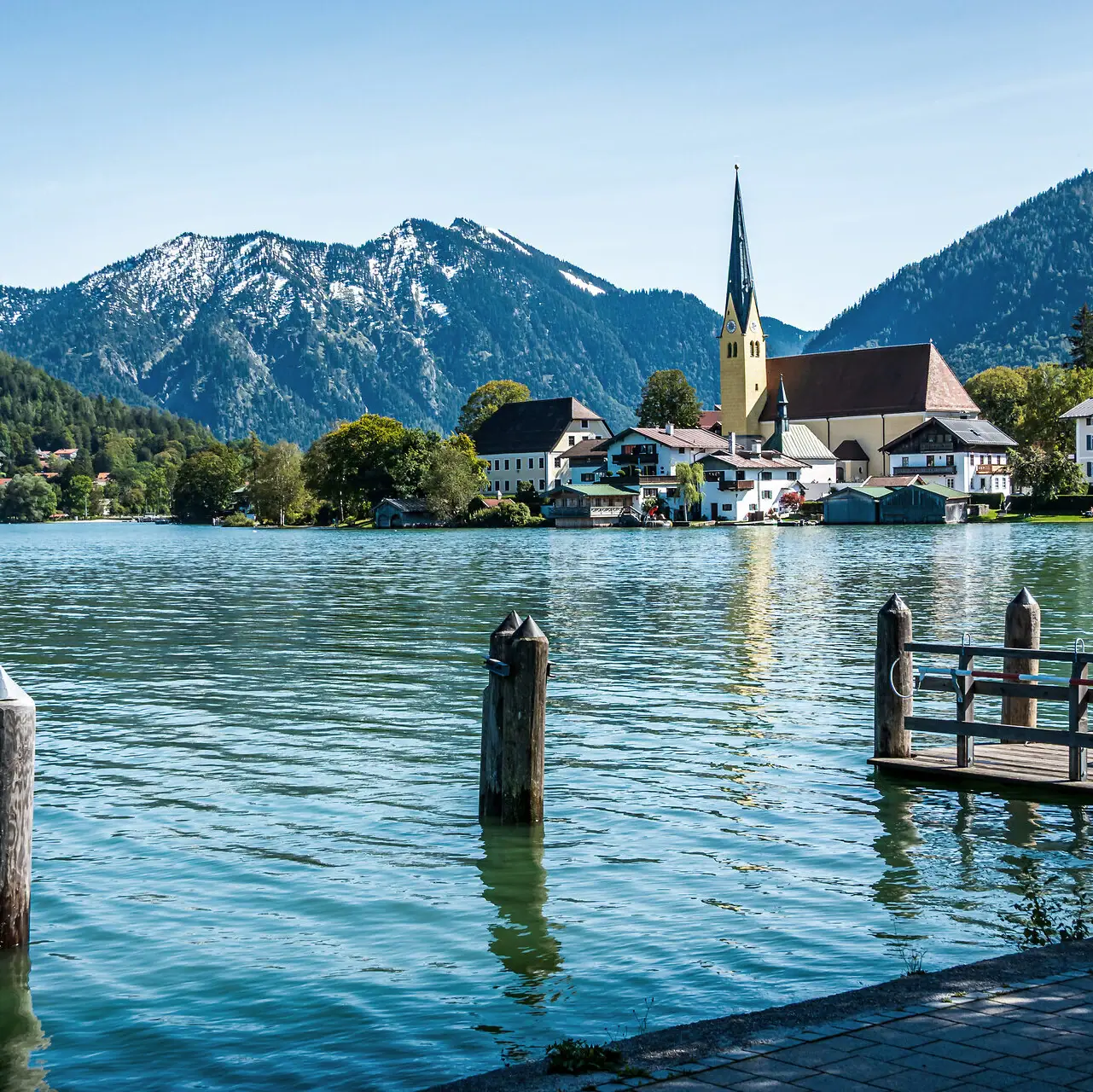 Il lago Tegernsee con una chiesa e le montagne sullo sfondo.